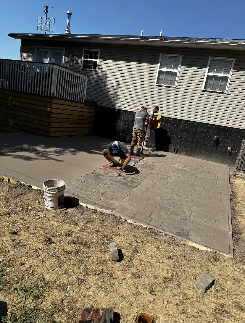 Crew installing pavers on a new concrete base behind a home